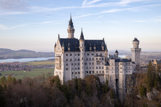 Bavaria, Germany. Fairytale Neuschwanstein Castle in Bavarian Alps mountains. Picturesque view at green forest trees, lake sunrise sky with clouds
