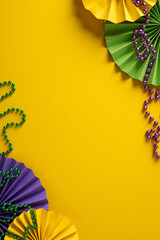Obraz premium Vibrant vertical Mardi Gras themed scene features purple, green, and gold fans and bead garlands arranged on a bold yellow background, conveying festive energy and a lively greeting for events