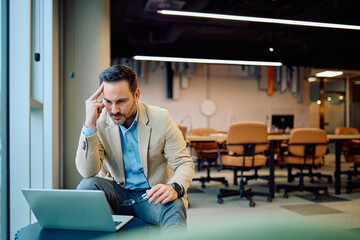 Focused businessman working on his laptop, deeply concentrating and problem solving in a modern corporate office setting