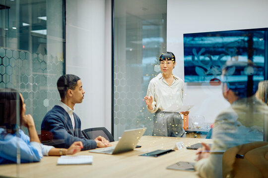 Asian businesswoman presenting ideas and leading discussion with diverse colleagues in a modern corporate boardroom meeting