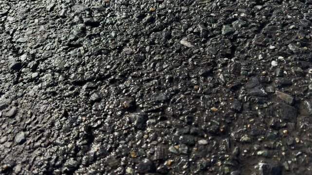 Wet asphalt texture close-up, rain-soaked pavement surface with water film