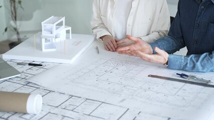 Engineering professionals collaborating on an architectural blueprint, using a compass to design a modern building, planning construction with a house model and laptop