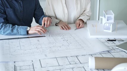 Engineering professionals collaborating on an architectural blueprint, using a compass to design a modern building, planning construction with a house model and laptop