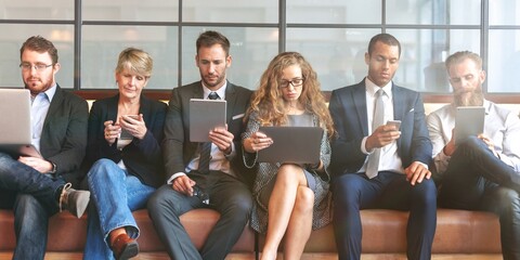 Group of professionals sitting on a couch, using laptops and tablets. Diverse team in business, focused on technology and communication. Business professionals using devices, using social media