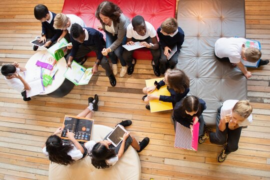 A diverse group of children, boys and girls, with a female teacher, engaged in learning activities. The children, of various ethnicities, are reading and writing together. Elementary school education.
