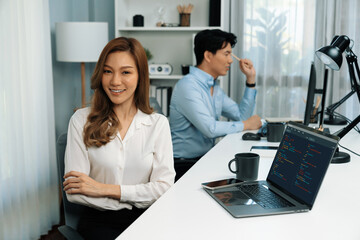 Profile smiling beautiful Asian businesswoman looking camera to portrait pose at modern office on working desk casual day. Blurry background man colleague analyzing data market plan on pc. Infobahn.