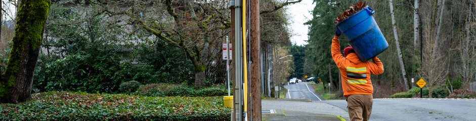 City landscaping maintenance worker carrying a garbage can full of dry fall leaves, cleanup of public space  © knelson20