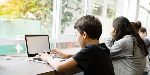 Young boy using laptop by window. Boy typing, learning, and exploring. Technology and education for young boy. Bright, natural light setting. Students learning on laptops, computer class