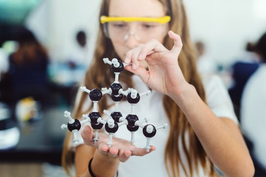 Young girl in a science lab holding a molecular model. The girl is focused on the molecular model. Science lab setting with a girl and a molecular model. Elementary school science education. - Powered by Adobe