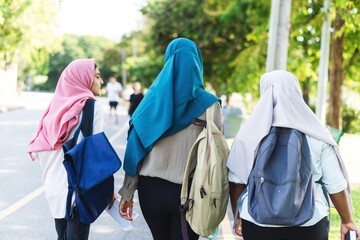 Three Muslim giel students walking outdoors with backpacks and colorful hijabs. Happy Muslim girl...