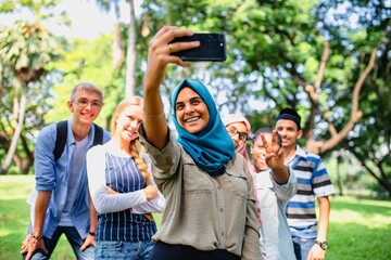 Obraz premium Group of young adults taking a selfie outdoors. Diverse friends smiling, enjoying nature. Casual attire, sunny day, happy moments captured in a park setting. International students taking selfie.