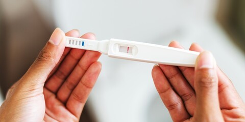 Close-up of hands holding a pregnancy test with a positive result. The test shows two lines. Positive pregnancy test in focus, indicating pregnancy confirmation. Woman holding negative pregnancy test.