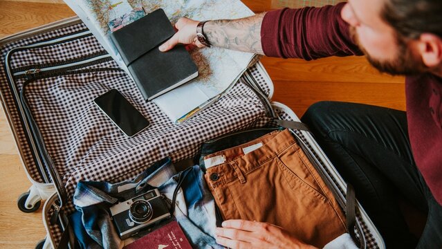 Man packing suitcase with clothes, map, and camera. Travel essentials like map, camera, and clothes are organized. Preparing for travel with essentials packed. Man getting ready to travel.