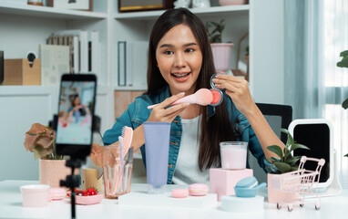 Young beautiful Asian reviewing cosmetic makeup brush cheek testing collection with pastel color, showing glow blusher mood with pink to promote on social media online recording smartphone. Stratagem.