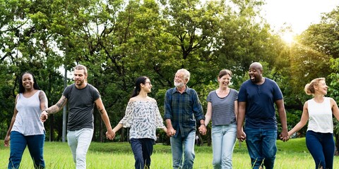 Diverse group of friends hold hands at park. Diverse group of men and women standing together hold...