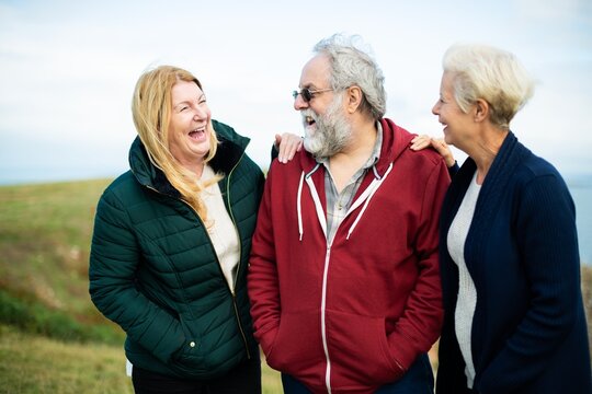 Three eldery adults laughing outdoors. Two old women and one senior man enjoying nature. Happy seniors in casual clothing, sharing a joyful moment in a grassy field. Happy old people enjoying nature.