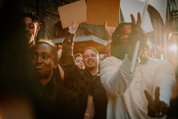 Diverse group of happy people holding protest signs. Group of various ethnicity people united in protest. Protest signs raised by people. Diverse group of happy people in protest with blank paper sign