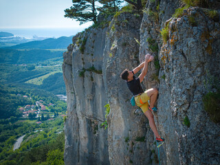 Focused male rock climber lead climbing a vertical limestone cliff in Osp with a stunning Karst...