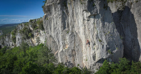AERIAL: Rock climber scales a tall limestone face in the famous Osp climbing area. Shirtless man...