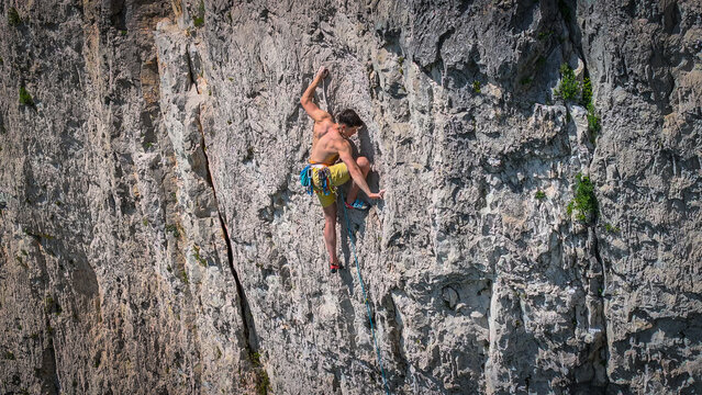 Shirtless climber searches for a foothold as he climbs a difficult route in famous Osp climbing area. Belayed man is lead climbing a steep limestone wall on a hot day. Adrenaline outdoor activity.