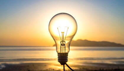 A lightbulb silhouette at sunset, its filament brightly lit by the setting sun, with ocean and land in the soft-focused background