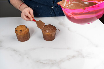 A pastry chef covering small panettone cakes with melted chocolate.