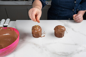 A pastry chef placing chopped pistachios on top of the small panettone cakes.