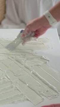 Vertical video: Placing paste, artist pulling palette knife across home canvas, texturing surface