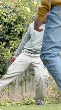 Vertical video: Walking guy in sweater crossing frame, friend tapping soccer ball in yard to play