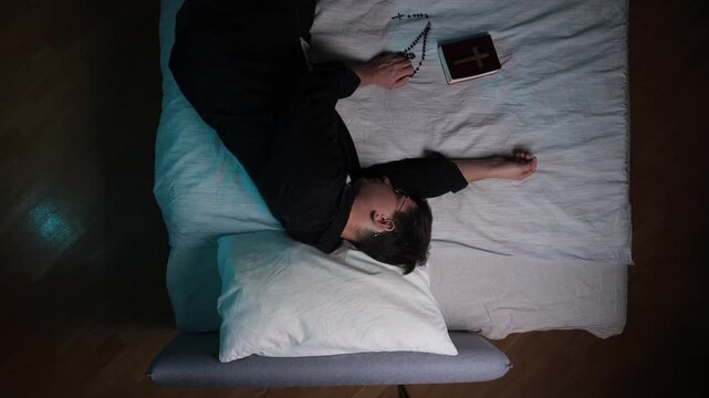 Exhausted priest finding peace, resting on a bed with a bible and rosary beads beside him, reflecting a moment of spiritual contemplation or rest after long devotion