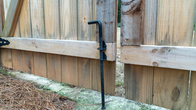 Black metal drop rod gate latch or cane bolt installed on a wooden privacy fence for secure backyard access and residential property enclosure and home safety maintenance concepts.