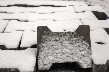 Close-up of concrete paving blocks covered with fresh snow, forming a geometric urban pattern. Minimalist winter background with strong texture and copy space