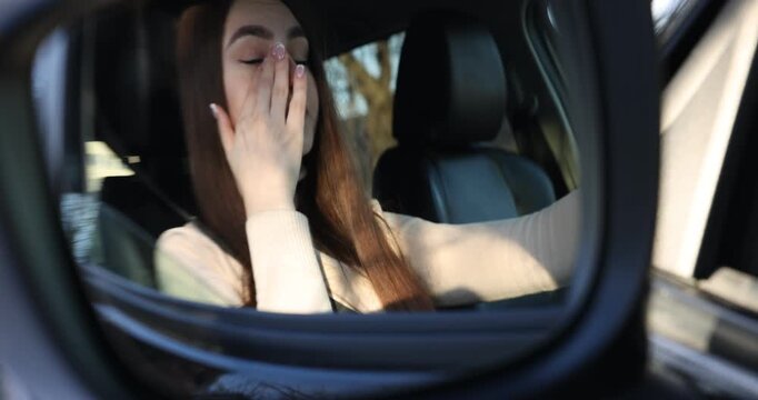 Woman feeling fatigue in her modern auto, view through car side mirror. Camera moving in