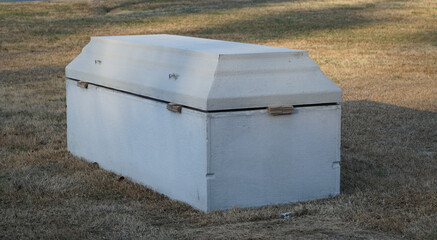 Concrete burial vault or grave liner in a green cemetery field for funeral service concepts