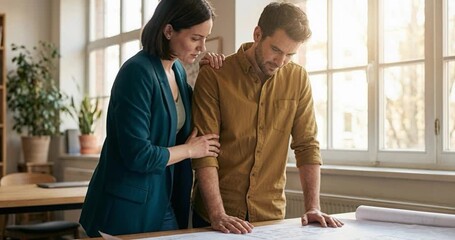 Two professionals collaborating over a blueprint in a bright office space