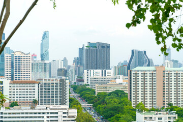 Elevated view of Bangkok cityscape featuring modern skyscrapers like MahaNakhon and lush green urban parks. High-angle perspective of city traffic and architectural diversity in Thailand.