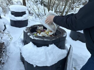 Adding food scraps to outdoor compost bin in snowy garden &ndash; sustainable winter lifestyle in practice