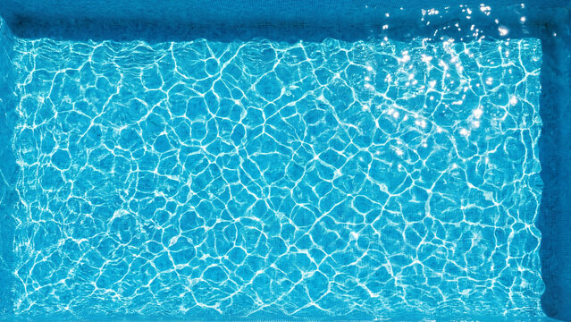 Blue swimming pool water surface texture with sun reflections and ripples.
