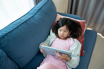 Young Asian Girl Relaxing on a Sofa and Playing or Watching a Tablet Computer