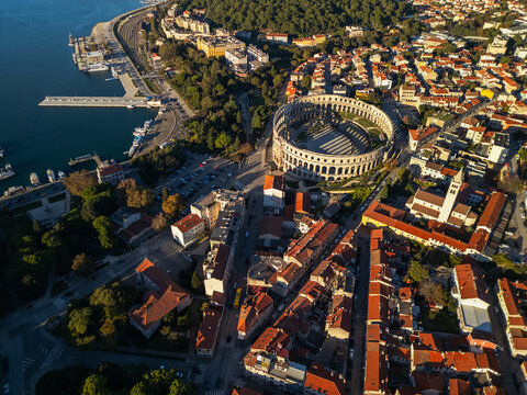 Epic aerial view of Pula Arena Roman amphitheater at sunset. Panoramic cityscape of Pula with historic landmarks and harbor, Croatia.