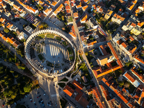 Pula Arena ancient Roman amphitheater with historic city skyline and orange roofs aerial drone view.
