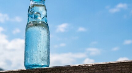 Ramune soda bottle with marble, condensation on glass, blue sky background. copy space for text
