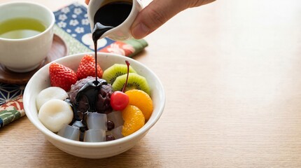 Anmitsu dessert bowl with agar jelly and fruit, pouring black syrup. copy space for text
