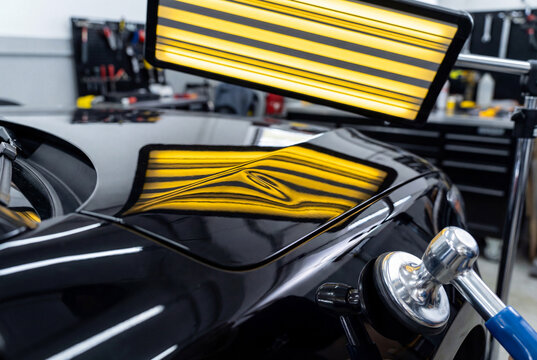 Specialist performing paintless dent repair PDR on car door checking reflection in line board