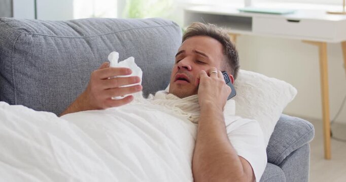 Man sick with virus cold fever on couch. Holding tissue and phone at home, showing flu symptoms, telehealth guidance and self care for marketing. Clear illness and remote care concept.