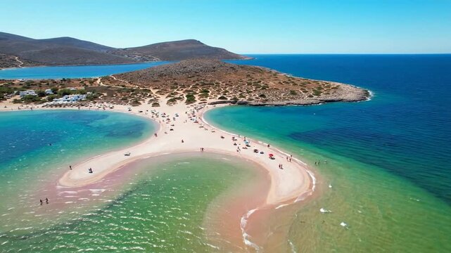 Aerial view of a unique sandy tombolo beach with people, vivid blue-green waters, and distant hills