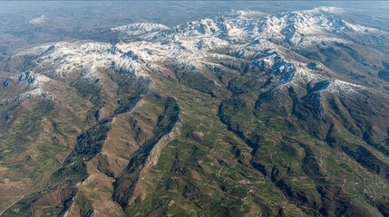 Aerial View of Snow Capped Green Mountain Range Landscape with Dense Forests and Clear Blue Sky Scenic Outdoors in Natural Sunlight
