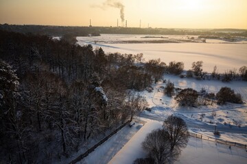 Golden hour casts a magical glow over a sprawling snowy forest and frozen river. A tranquil winter vista from above, pristine and captivating