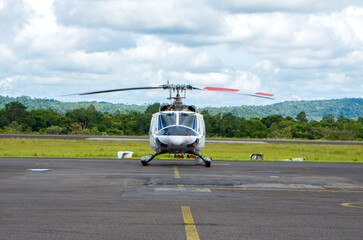 Stationary helicopter on the runway at Tanjung Pandan Airport, Belitung. An aircraft parked on the apron surrounded by green trees and a cloudy sky.