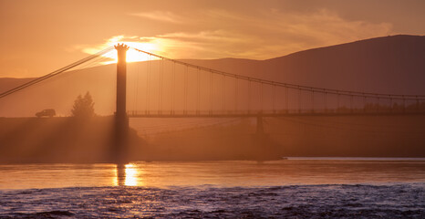 Obraz premium Bridge over the river against the backdrop of a bright sunset, summer travel